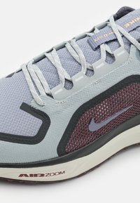Scarpa sportiva Nike con tomaia in mesh grigio chiaro e dettagli in grigio scuro e bordeaux, lacci piatti e suola Air Zoom ammortizzata.