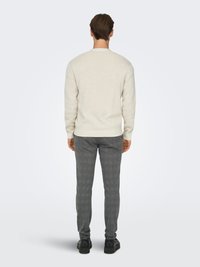 Pull en maille beige clair à col rond, associé à un pantalon gris foncé à carreaux et des chaussures noires. Texture douce, coupe ajustée, longueur standard.