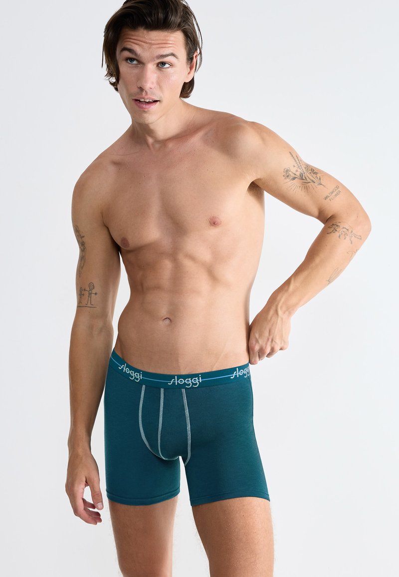 Teal herenboxers met een nauwsluitende pasvorm. Zachte stof, elastische tailleband met daarop het witte "Sloggi"-logo en contrasterende stiksels.