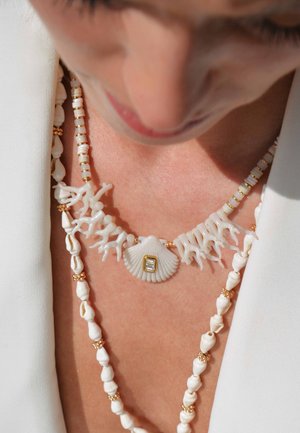 Collier en corail blanc avec pendentif en coquillage, accents dorés et petits détails en perles. Présente des formes de corail texturées et des agencements de perles variés.