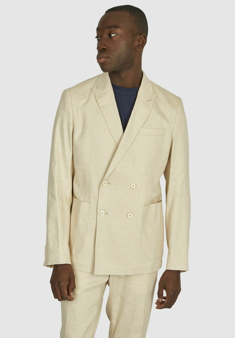 Beige linnen dubbelzijdig colbert met twee voorkeurszakken en lichte knopen. Getextureerde stof, getailleerde pasvorm, en met nietjes revers.