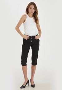 Pantalons cropped noirs avec un devant boutonné, en tissu texturé et dotés de poches latérales, associés à un débardeur blanc ajusté et des talons noirs.