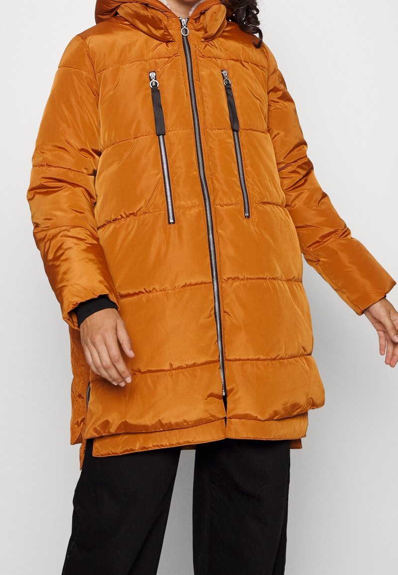 Oranssi puhvitakki hupulla, jossa on mustat vetskarit ja kaksi etutaskua, kiiltävän, tikatun pinnan kanssa.