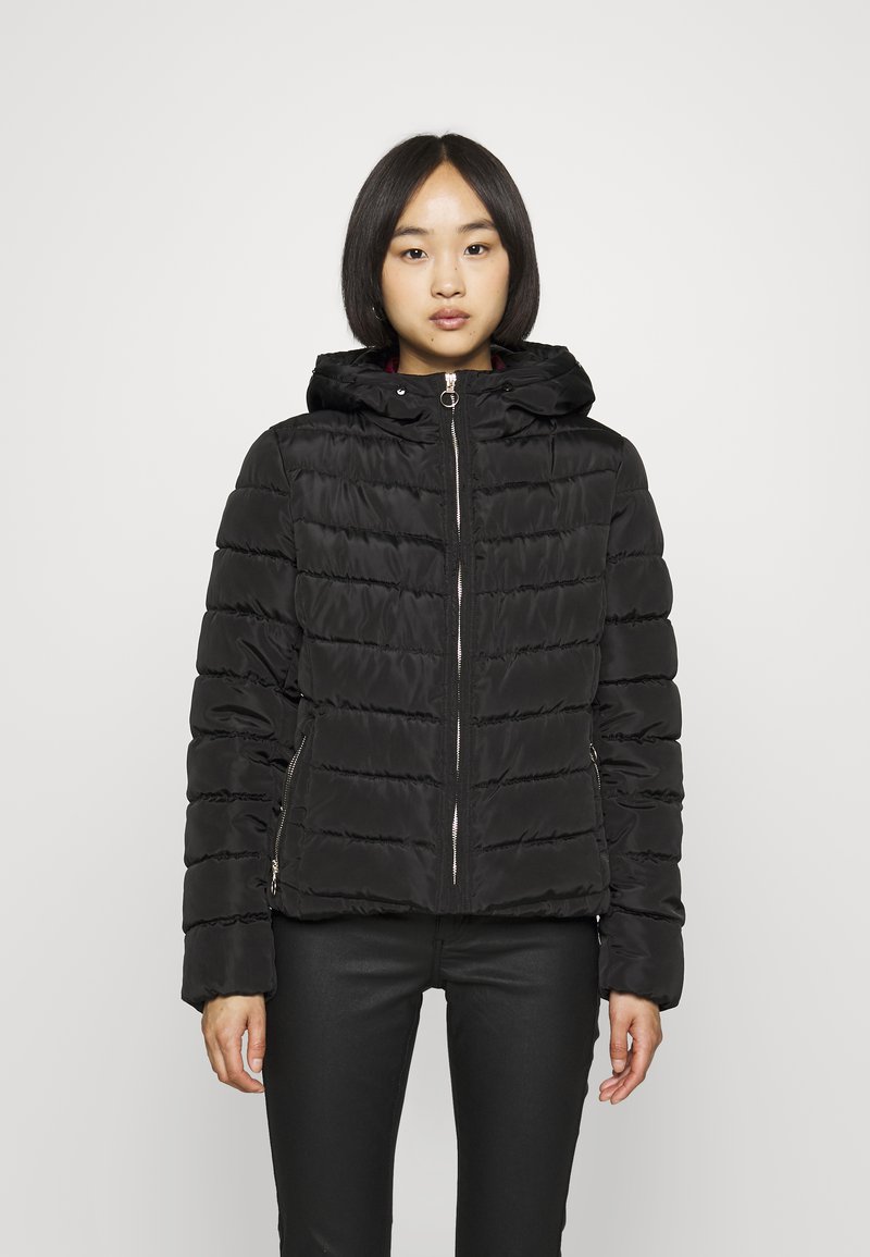 Giacca a vento nera con cappuccio, caratterizzata da un design trapuntato, cerniera anteriore e tasche laterali. Texture liscia e silhouette affusolata.