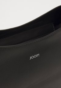 Svart lærveske med en subtil preget logo som leser "JOOP!" nær den øvre kanten, som viser et elegant og minimalistisk design.