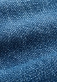 Tuvplāns zilas džinsa auduma ar redzamu pinuma tekstūru un nelielām ēnojuma un kroku variācijām.