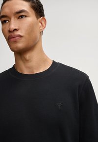 Schwarzes Sweatshirt mit Rundhalsausschnitt, gerippten Bündchen und einem kleinen, gestickten Blumenlogo auf der Brust. Glattes, Baumwollmischgewebe.