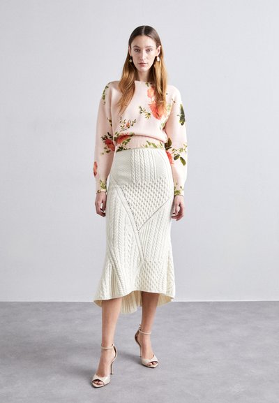 Pink floral sweater with long sleeves, paired with a white knit midi skirt featuring textured patterns and a high-low hemline. Beige heels.
