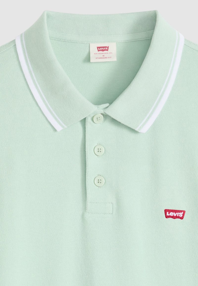 Hellgrünes Levi's-Poloshirt mit weißen Doppelstreifen am Kragen, drei Knöpfen und einem roten Levi's-Logo auf der Brust.