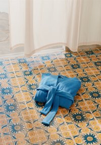 Türkiis sinine pehme kangast hommikumantel, korralikult volditud koos vööga, asetatud mustriga plaatpõrandale, millel on kollased ja sinised lillemustrid.