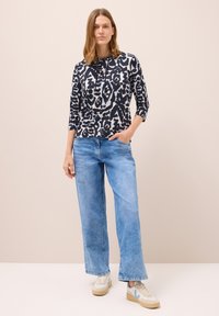 Camisa de manga larga a rayas en blanco y negro con capucha, combinada con unos pantalones vaqueros de pierna ancha en azul claro y zapatillas beige con detalles en azul.
