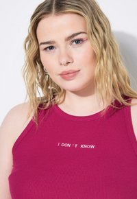 Top a maniche corte aderente in rosa scuro con scollatura rotonda e testo ricamato bianco "NON LO SO" centrato sul petto.