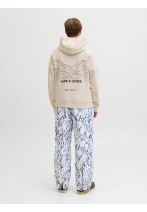 Beige hoodie met een omlijnd bergontwerp op de achterkant, gecombineerd met loszittende witte broek met een blauw gemarmerd patroon.