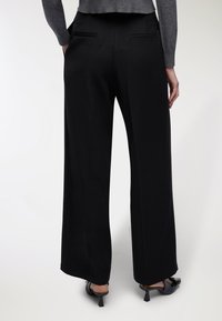 Pantaloni neri a gamba larga realizzati in tessuto liscio, con tasche posteriori, vestibilità rilassata e orlo che si ferma sopra la caviglia.