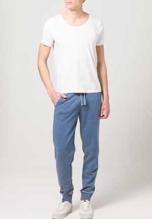 White short-sleeve t-shirt paired with blue jogger pants featuring an elastic waistband and cuffed ankles, worn with white sneakers.