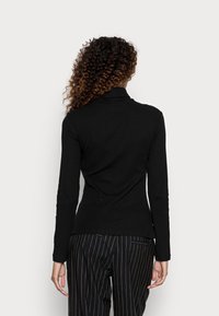 Musta ribattu pitkähihaine paita, jossa on kaulus, ja se on muotoiltu tiukasti. Materiaali näyttää pehmeältä ja siinä on hienovarainen tekstuuri.