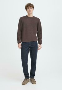 Suéter de punto marrón con textura, jeans azul oscuro y zapatos marrones claros. El suéter tiene un cuello redondo y mangas largas.