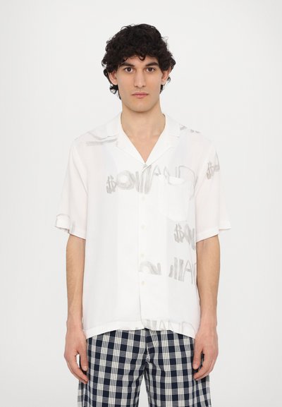 White short-sleeve shirt with gray dollar sign print, single chest pocket, and buttons. Paired with checkered blue and white pants.