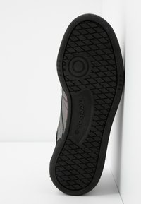 Semelle de basket Reebok noire avec un motif de bande de roulement circulaire et le logo "Reebok" embossé au centre, présentée sur un fond blanc.