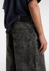 Pantalones cortos de mezclilla desgastada en negro y gris con un parche de tablero de ajedrez en la cintura, cinco bolsillos y un ajuste holgado.