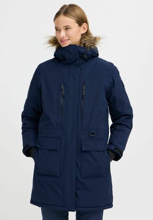 Mørkeblå parka-jakke med hette foret med pels, flere glidelåslommer og lapper, samt et stilrent design. Vanntett, isolert og slitesterkt stoff.