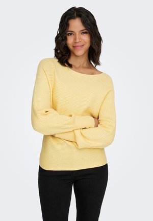 Yellow ribbed sweater with a wide neckline and long sleeves, crafted from soft fabric, worn with black pants, arms crossed.