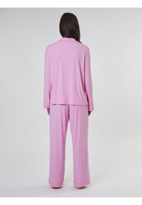 Conjunto de loungewear rosa que consiste en una parte superior de manga larga con cuello y pantalones de pierna ancha a juego, fabricado en una tela suave y ligera.