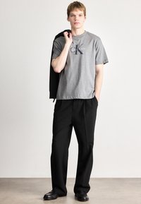 Γκρι βαμβακερή μπλούζα τύπου t-shirt με λογότυπο Calvin Klein, συνδυασμένη με φαρδιά μαύρα παντελόνια και μαύρα παπούτσια; casual στυλ, απαλή υφή.