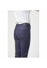 Marineblauwe slim-fit broek met een gladde textuur, voorzien van achterzakken en een leren label op de tailleband. Eenvoudig, functioneel ontwerp.