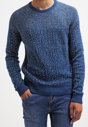 Pull en tricot bleu avec un motif blanc moucheté, col rond et poignets et ourlet côtelés. Coupe ajustée avec une finition texturée.
