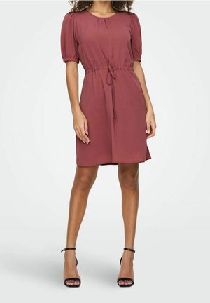 Woman wearing a knee-length dusty rose dress with puffed short sleeves, a drawstring waist, and black ankle-strap high heels.
