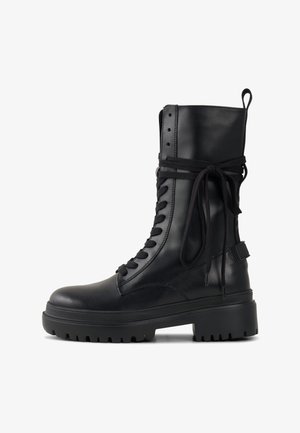 Černá kožená kotníková bota se šněrováním, robustní podrážkou, texturovanými detaily a látkovým páskem kolem horní části. Má poutko na uchopení.