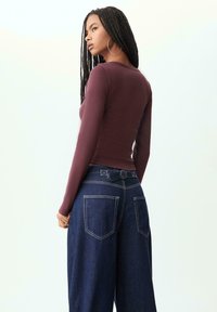 Burgundy long-sleeve top paired with wide-leg dark denim jeans. The top features a round neckline and fitted silhouette. Jeans have large back pockets.