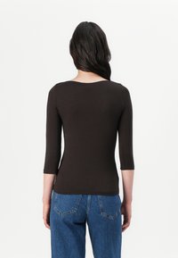 Brun, tettsittende topp med rund halslinje og trekvart lange ermer, sammen med høytlivs blå jeans. Glatt tekstur, minimal detaljering.
