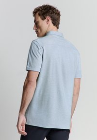 Himmelblaues Polohemd mit kurzen Ärmeln aus einem strukturierten Stoff, mit einem weichen Kragen und einer entspannten Passform sowie einem geraden Saum.