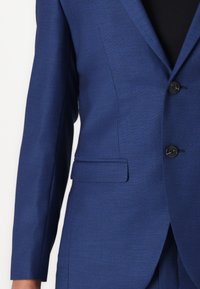 Blazer bleu ajusté avec une texture lisse, des revers crantés, deux poches frontales et trois boutons noirs à l'avant.