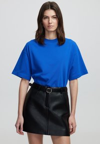 Koningblauwe katoenen t-shirt met een ronde hals en korte mouwen, gecombineerd met een zwarte neplederen minirok en een zwarte riem met een zilveren gesp.