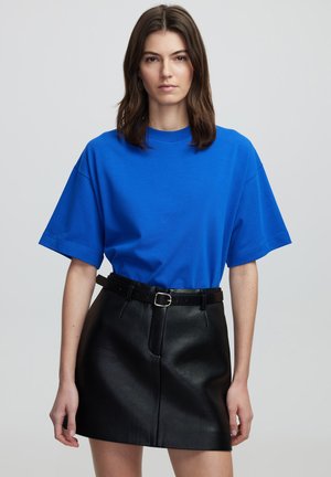 Koningblauwe katoenen t-shirt met een ronde hals en korte mouwen, gecombineerd met een zwarte neplederen minirok en een zwarte riem met een zilveren gesp.
