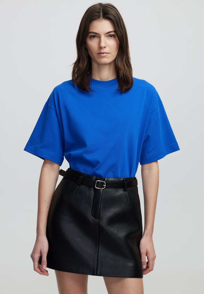 Koningblauwe katoenen t-shirt met een ronde hals en korte mouwen, gecombineerd met een zwarte neplederen minirok en een zwarte riem met een zilveren gesp.