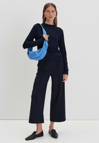 Navy Blau Langarmoberteil kombiniert mit weit geschnittenen Hosen. Das Model trägt eine weiche, hellblaue Handtasche und flache schwarze Schuhe. Minimalistisches Design.