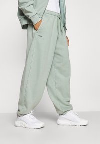 Ljust gröna, löst sittande träningsoverallbyxor i mjukt tyg med elastisk midja och sidfickor, matchat med vita sportskor.