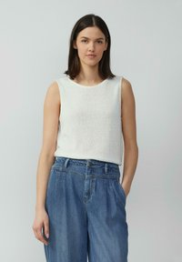 Haut sans manches blanc en tissu texturé avec un col rond, associé à un jean en denim bleu ample avec des poches latérales.