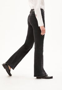 Black flared jeans made of denim, featuring a slight fade, five-pocket design, and a clean hem, paired with black loafers.