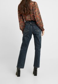 Jeans blu scuri a vita alta con gamba dritta, realizzati in denim, caratterizzati da un orlo leggermente sfilacciato e un design a cinque tasche.