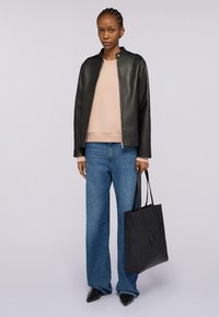 Chaqueta de cuero negra con cuello alzado, sudadera rosa clara, vaqueros anchos azules y bolsa de tote negra. Zapatos negros de punta.