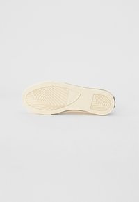 Sneakersula med en strukturerad gummimaterial, krämfärg, med ett zick-zack-mönster och märkets logotyp. Platt och utformad för bra grepp.