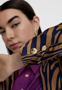 Long-sleeve shirt in brown and navy with a zebra stripe pattern, featuring gold buttons on the cuff and a purple collar.