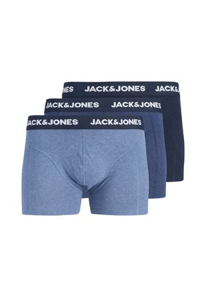 Mladý muž s krátkymi blond vlasmi stojí bez trička, má na sebe modré boxerky Jack & Jones na jednoduchom svetlom pozadí.