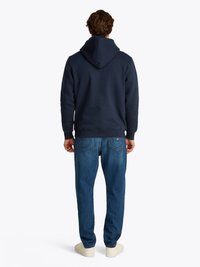 Navyblauwe hoodie met een trekkingkoord en een gestructureerde afwerking, gecombineerd met lichtblauwe jeans en witte sneakers, bekeken van achteren.