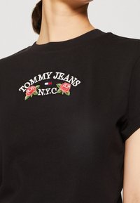 Černé bavlněné tričko s krátkým rukávem, zdobené vyšívaným nápisem "TOMMY JEANS N.Y.C." a designem růží v červené a zelené barvě.